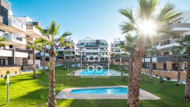 Et moderne hotel med swimmingpool omgivet af palmer og en velplejet græsplæne.