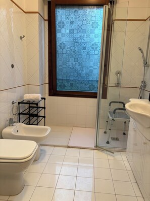 Un baño con dos lavamanos, un bidé, una ducha con puerta de vidrio y una ventana con vista decorada.