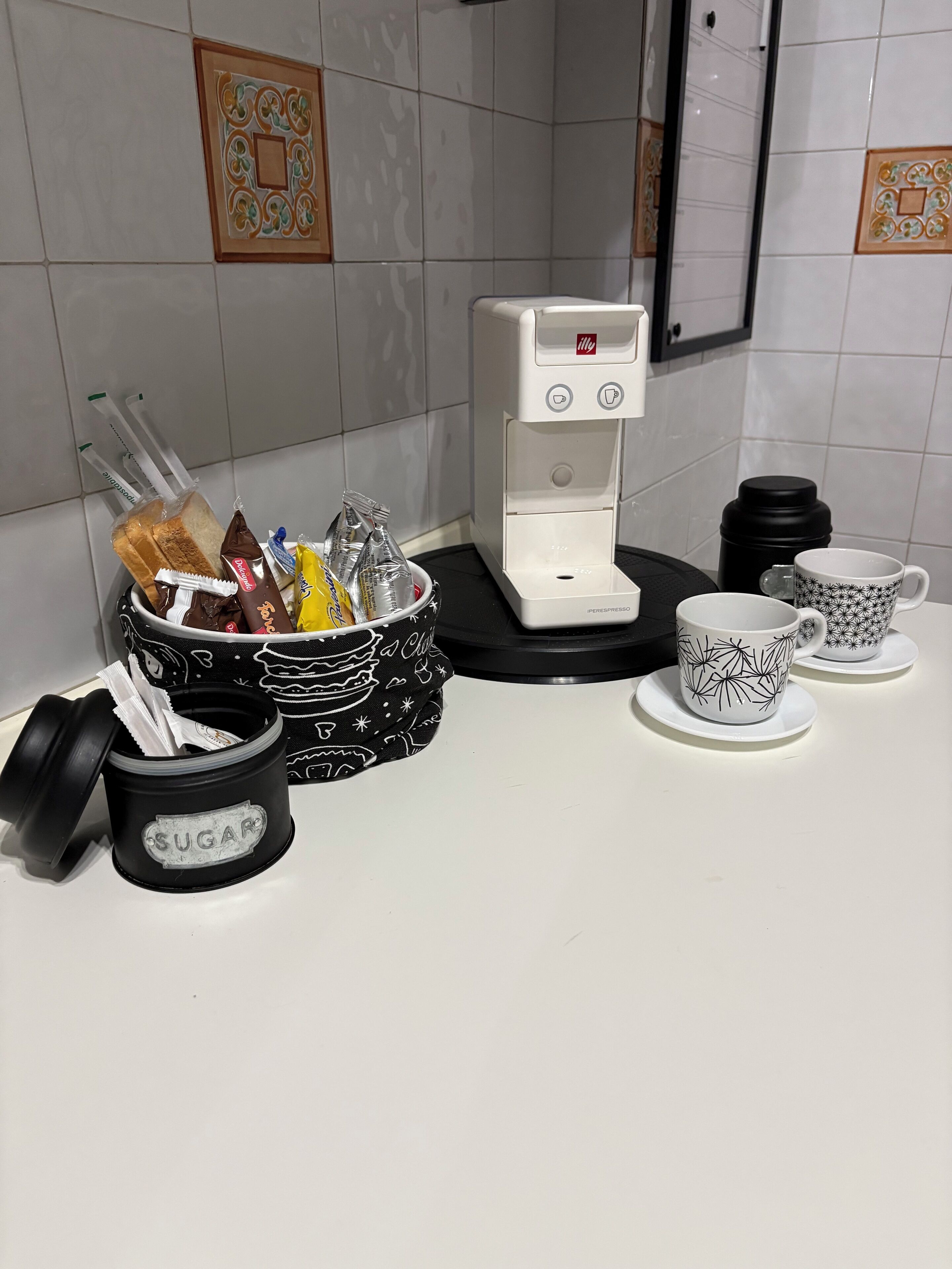 Eine Küchenarbeitsplatte mit Kaffeemaschine, Zuckerbehälter und Tassen.