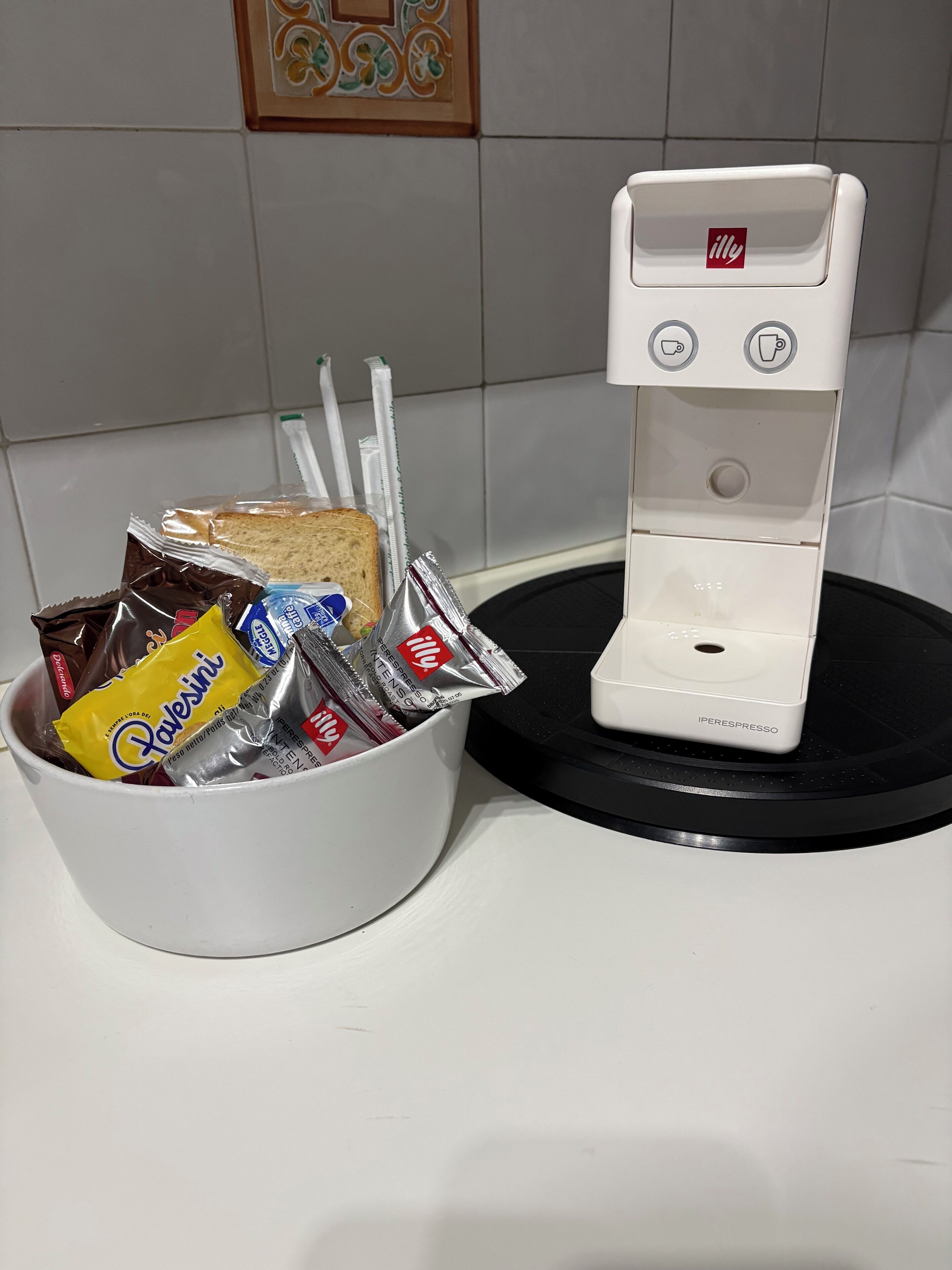 A coffee machine with a cup holder and a basket containing snacks and a chocolate bar.