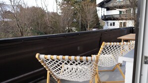 A balcony with two white wicker chairs and a wooden table.