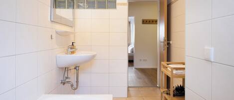A modern bathroom with a white sink, a bathtub, and a wooden shelf.