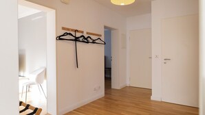 A hallway with wooden flooring, a coat rack with hangers, a white door, and a chair in the background.