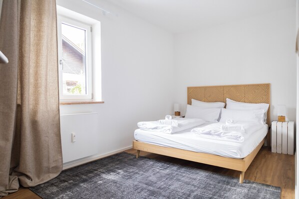 A neatly made bed with white linens, a wooden headboard, and a gray rug on the floor.