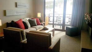 Ein Wohnzimmer mit Sofa, Sesseln, einem Couchtisch und Blick durch eine Glastür in einen Außenbereich.