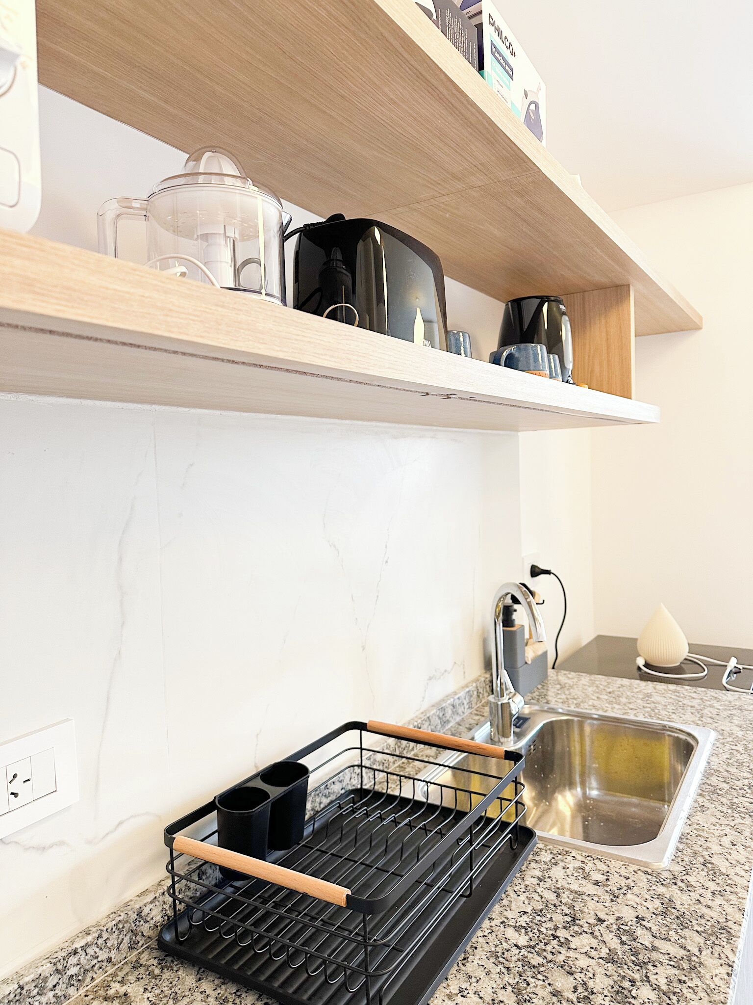 Una cocina con encimera de granito, pileta de acero inoxidable, escurreplatos negro y repisa de madera sobre la encimera.