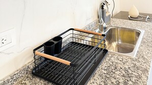 Een keuken met een granieten aanrecht, een roestvrijstalen spoelbak, een zwarte afwasschuurrek en een houten plank erboven.