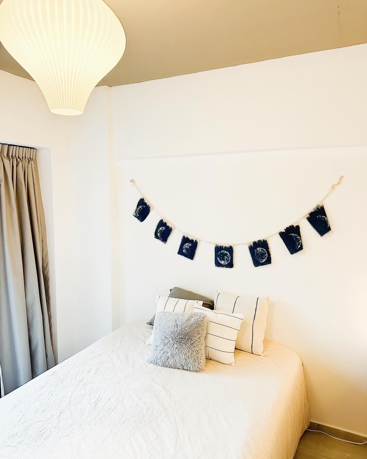 Ein Schlafzimmer mit einem Bett, Kissen, einer Bilderreihe in Schwarzweiß und einer weißen Deckenleuchte.