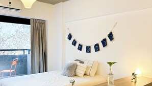 Een slaapkamer met een bed, een houten nachtkastje, een hanglamp, een raam met gordijnen en een decoratie aan de muur.