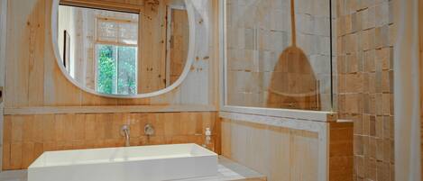 A bathroom with a wooden vanity, a large oval mirror, and a shower area.