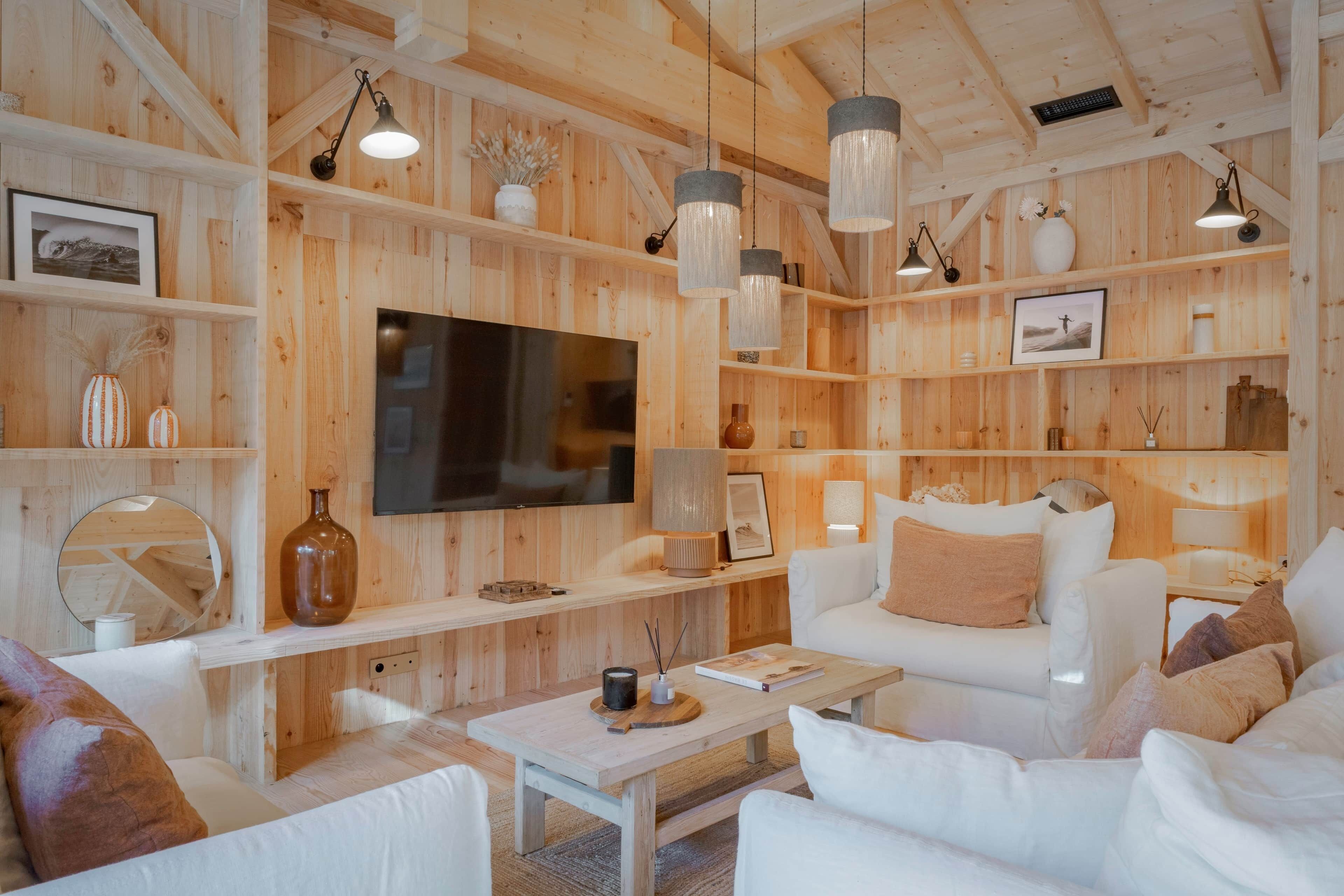 A modern living room with wooden paneling, white furniture, and pendant lighting.