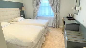 Een hotelkamer met twee bedden, een bureau, een spiegel en een raam met gordijnen.