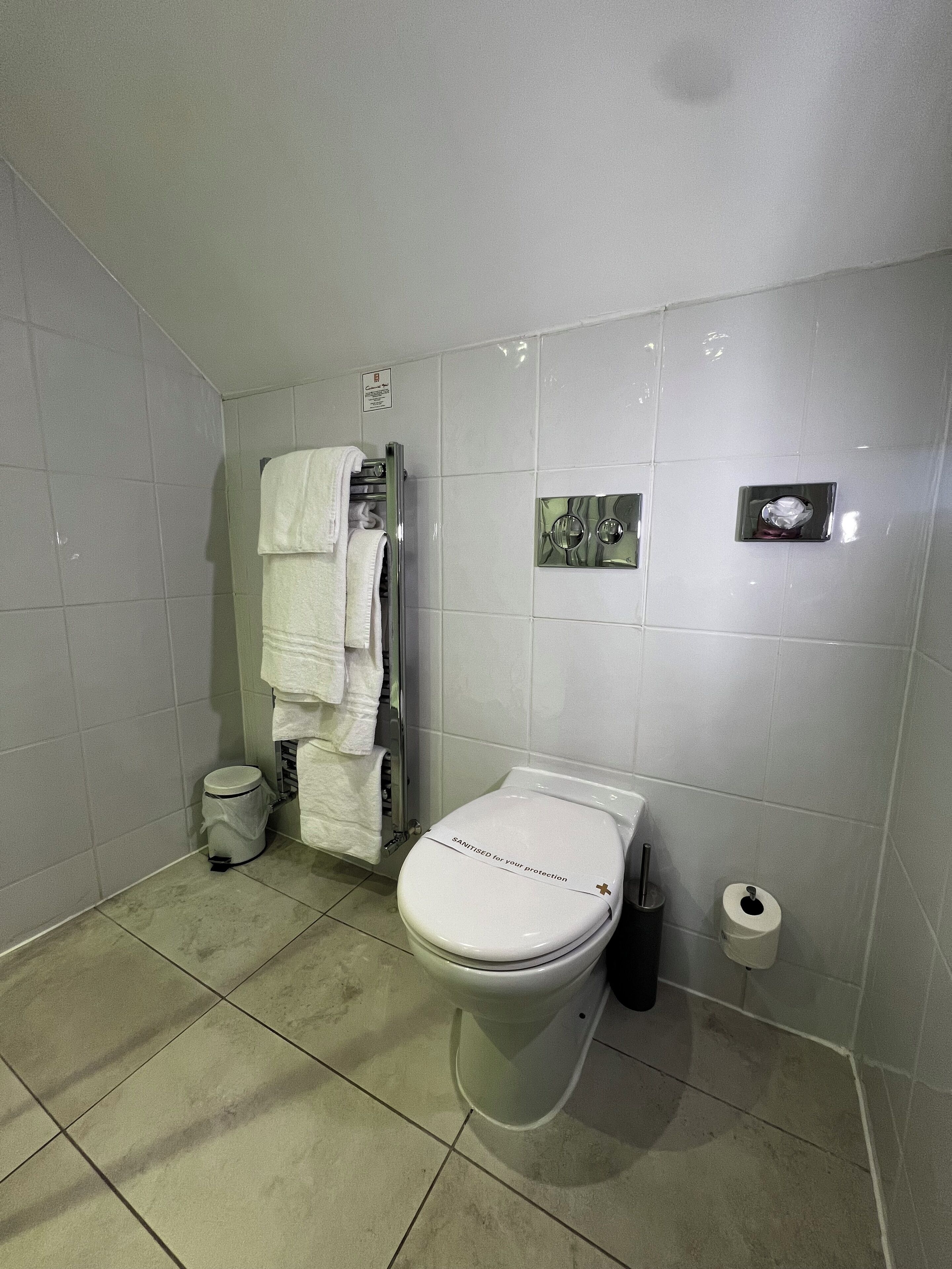 A bathroom with a toilet, a hand dryer, a trash bin, and a towel rack with multiple towels.