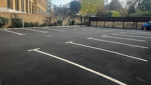 A parking lot with marked spaces, a blue car, and a building with large windows. - Centennial Hotel (Cambridge)