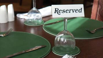 A dining table set with green placemats, a folded white napkin, a fork, a knife, and a glass dome. A sign reads 'Reserved.'