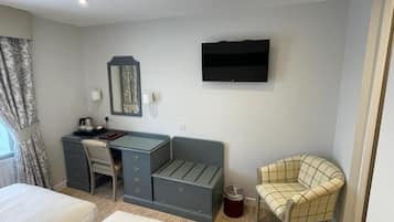 A hotel room with a bed, a desk with drawers, a chair, a TV mounted on the wall, and a window with curtains.
