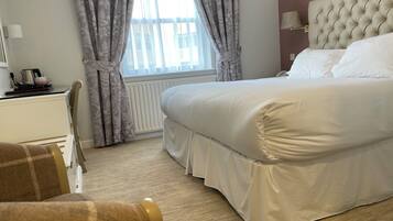A hotel room with a large bed, a desk with a kettle, and a chair.