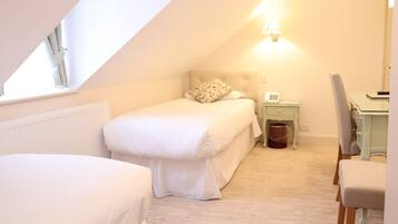 A small, well-lit bedroom with a single bed, a nightstand with a lamp, and a chair.