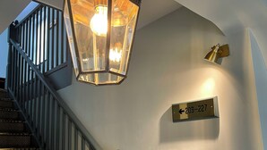 A staircase with a metal railing, a wall-mounted light fixture, and a directional sign indicating room numbers 209-227. - Centennial Hotel (Cambridge)
