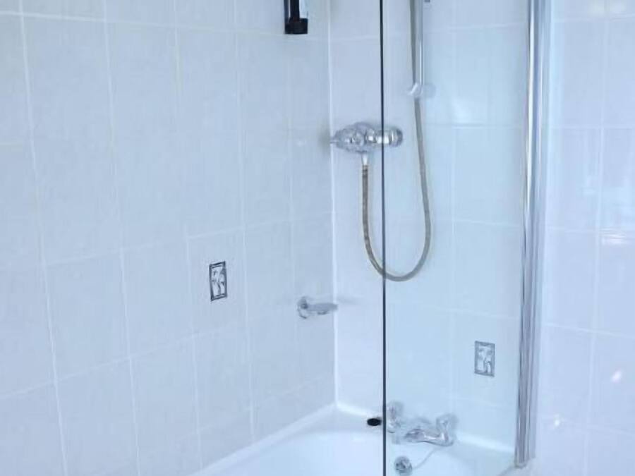 A modern bathroom with a glass-enclosed bathtub, a handheld showerhead, and a wall-mounted faucet.