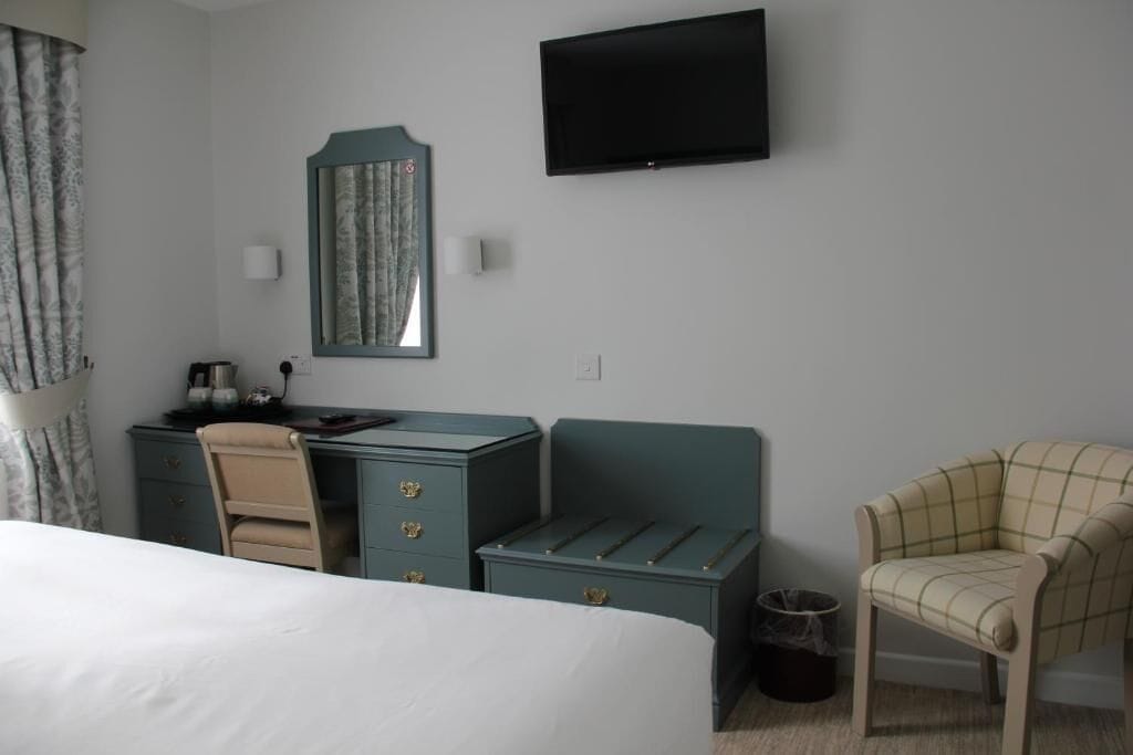 Habitación de hotel con cama, escritorio con cajones, silla, televisor montado en la pared y un cesto de basura pequeño.
