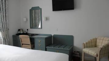 Habitación de hotel con cama, escritorio con cajones, silla, televisor montado en la pared y un cesto de basura pequeño.