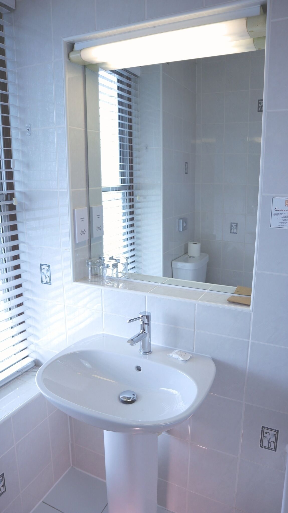 A bathroom with a white sink, mirror, and window with blinds.