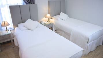 A hotel room with two single beds, a bedside table with a lamp, a phone, and a window with curtains.