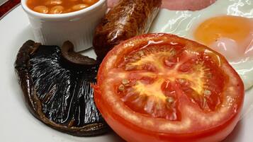 Ein Frühstücksteller mit Eiern, Würstchen, Speck, Bohnen und gegrillten Tomaten.