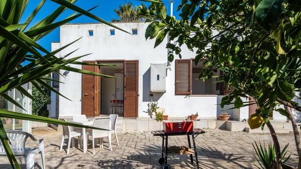 A patio with a table and chairs, a barbecue grill, and potted plants.