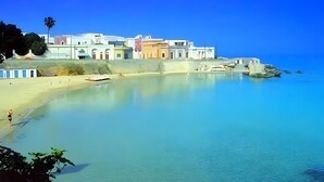 A coastal town with buildings along the shore, a sandy beach, and calm water.