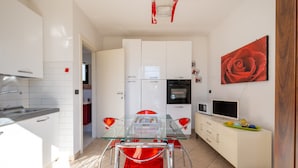 A modern kitchen with white cabinets, a glass dining table, and a red rose painting.