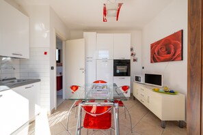 Cozinha moderna com armários brancos, uma mesa de jantar de vidro e uma pintura de uma rosa vermelha.