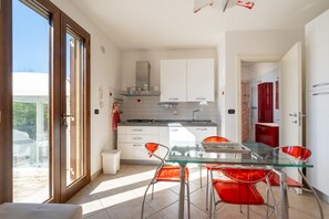 Une cuisine moderne avec des meubles blancs, une table à manger en verre et des chaises rouges.