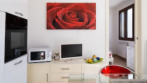 A modern kitchen with a microwave, oven, and a flat-screen TV on a white cabinet.