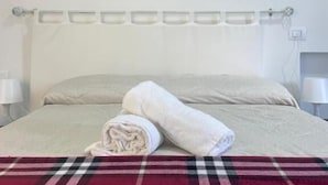 A bedroom with a bed, a red and black checkered blanket, a rolled white towel, and a painting of waves on the wall. - Beb sunset da Carla  (Agropoli)