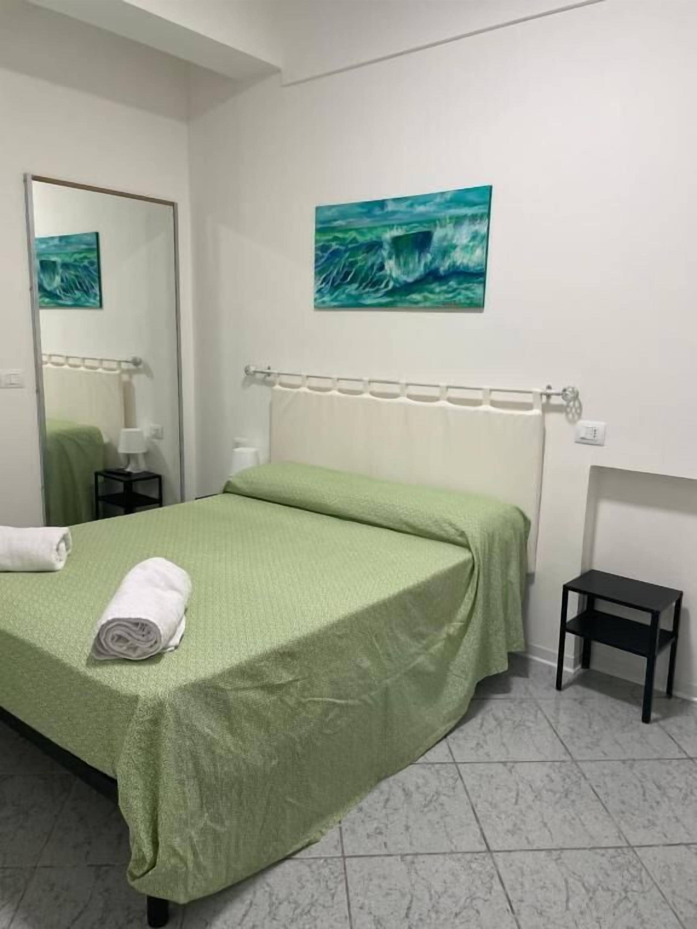 A hotel room with a bed, a small bedside table, a nightstand, a mirror, and a painting on the wall.