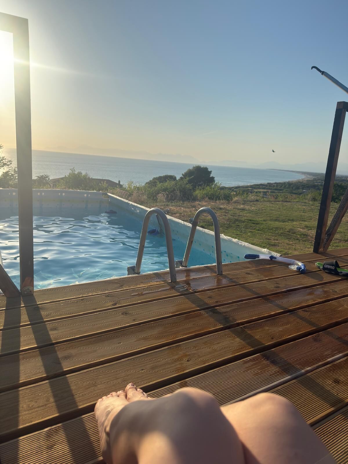 Un área junto a la piscina con vista al océano, una terraza de madera y una silla de descanso.
