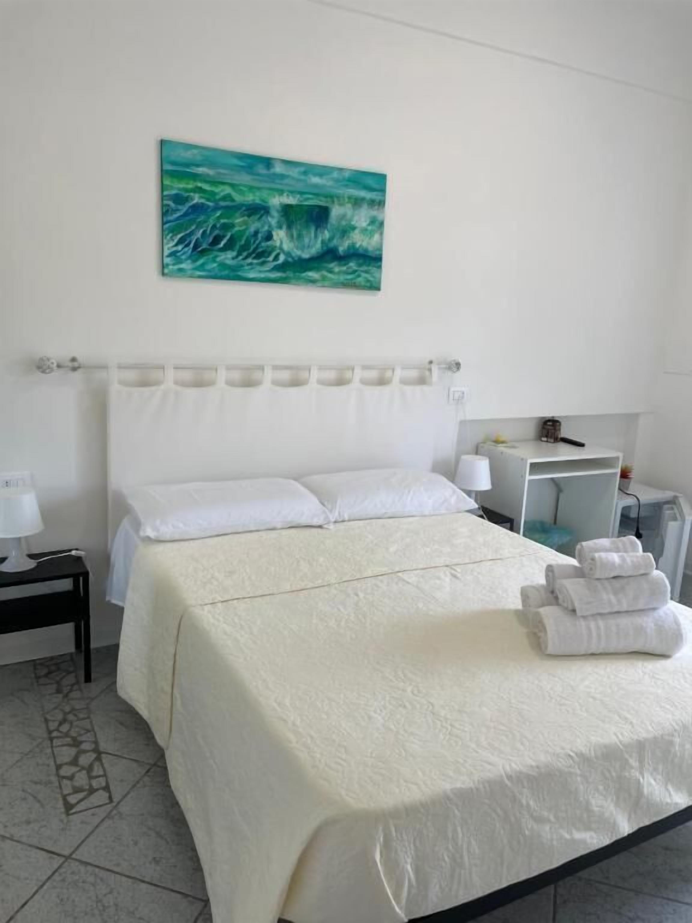 Habitación de hotel con cama, mesita de noche, un cuadro y zona de baño.