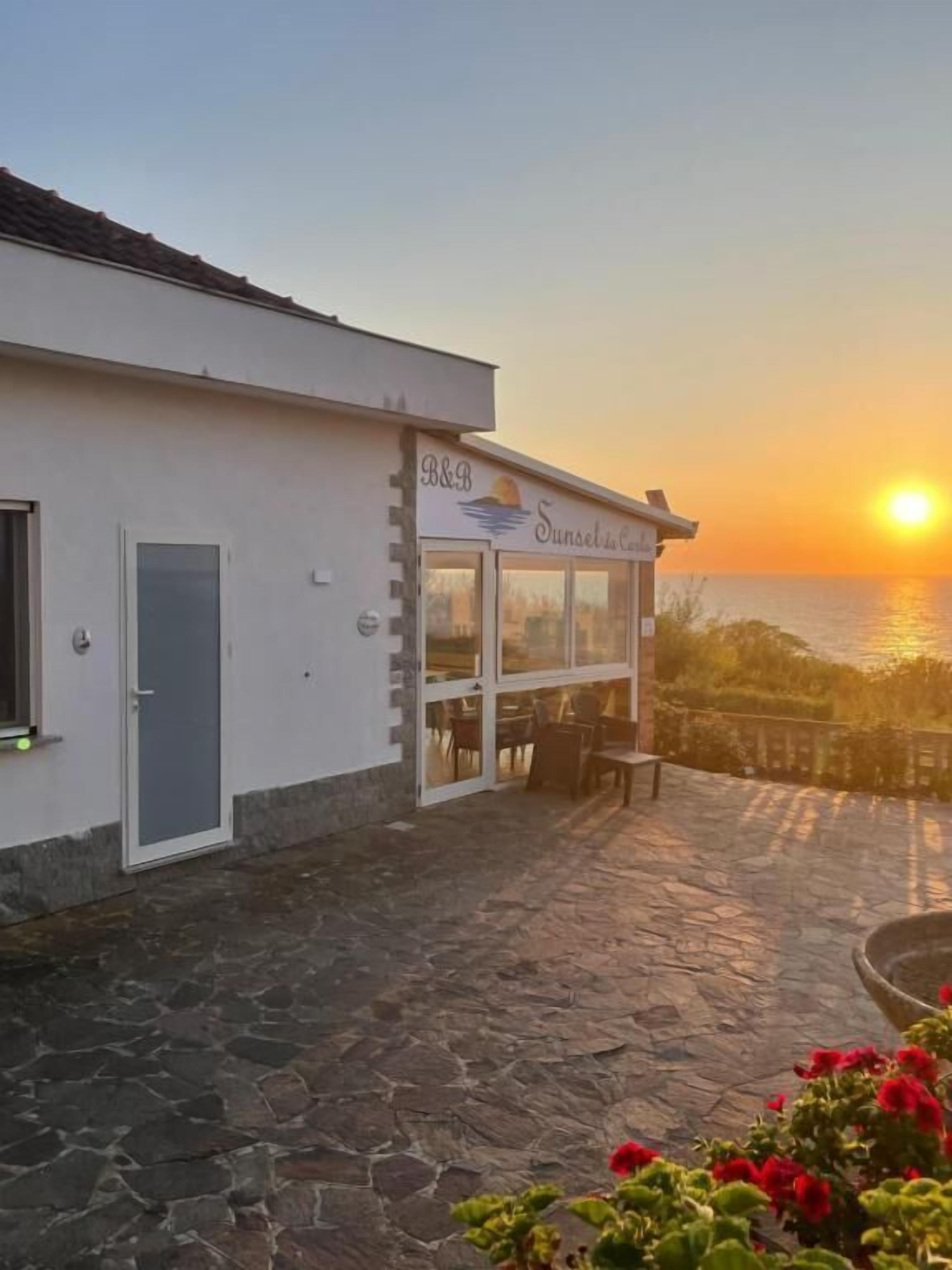 A building with a sign reading "B&B Sunset da Casa" with a view of the sunset over the ocean.