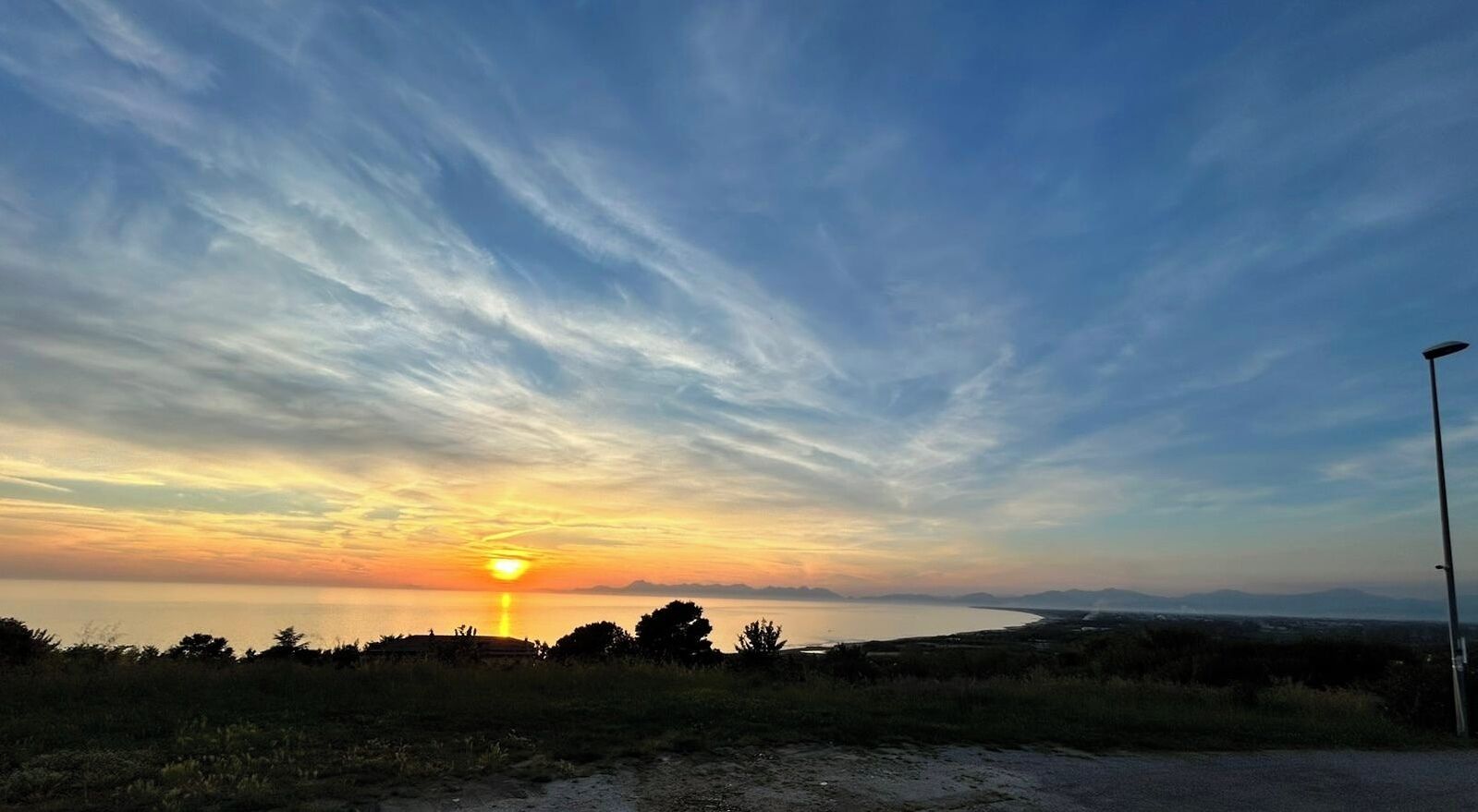 A sunset over a coastal landscape with a road and a streetlight.