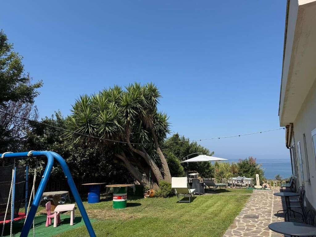 Un'area patio con altalena, tavolo e sedie, prato e vista sull'oceano.