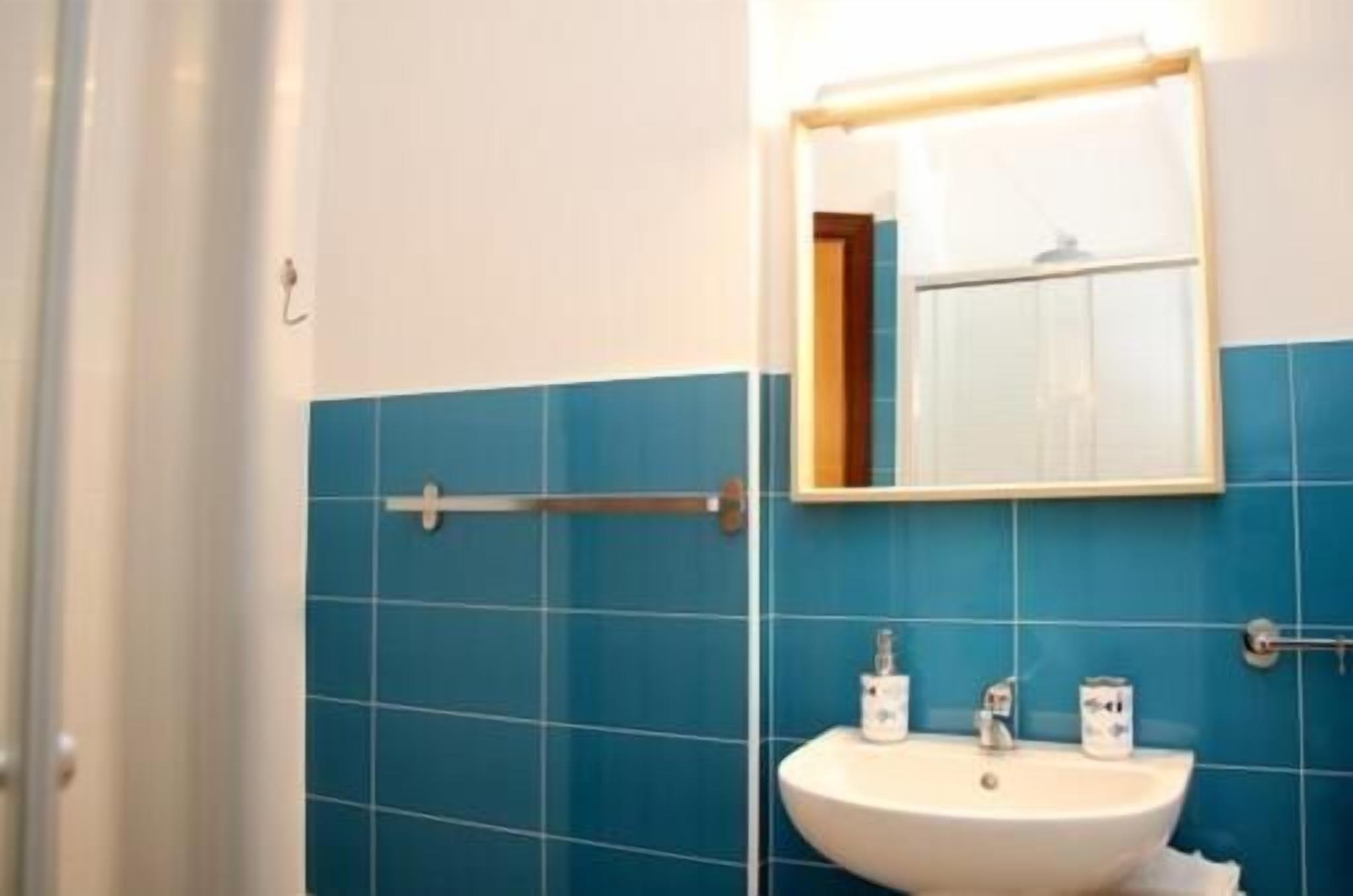 A bathroom with blue tiles, a white sink, and a mirror with a wooden frame.