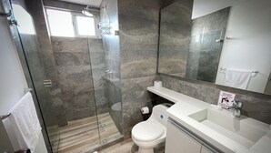 Ein modernes Badezimmer mit einer Duschkabine, einer Toilette und einem Waschbecken mit Spiegel.