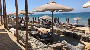 A beachside lounge area with stone walls, wooden lounge chairs, and large umbrellas providing shade. - Villa Marina Sea-Views with Private Pool (Peyia)