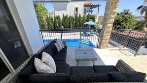 A balcony with a wicker sofa, a small table, and a pool in the background. - Villa Marina Sea-Views with Private Pool (Peyia)
