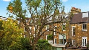 A residential building with multiple windows, a brick facade, and a tree in front. - Bright & Stylish Flat in the Heart of Islington (London)