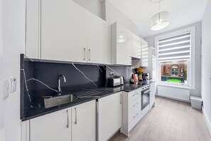 Eine moderne Küche mit weißen Schränken, einer schwarzen Arbeitsplatte und einem Fenster mit Jalousien.