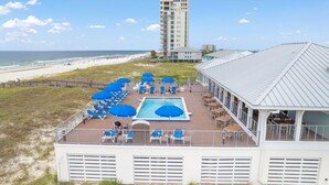 A rooftop pool area with blue umbrellas, lounge chairs, and a view of the beach and ocean. - Lost Key B203 (Pensacola)