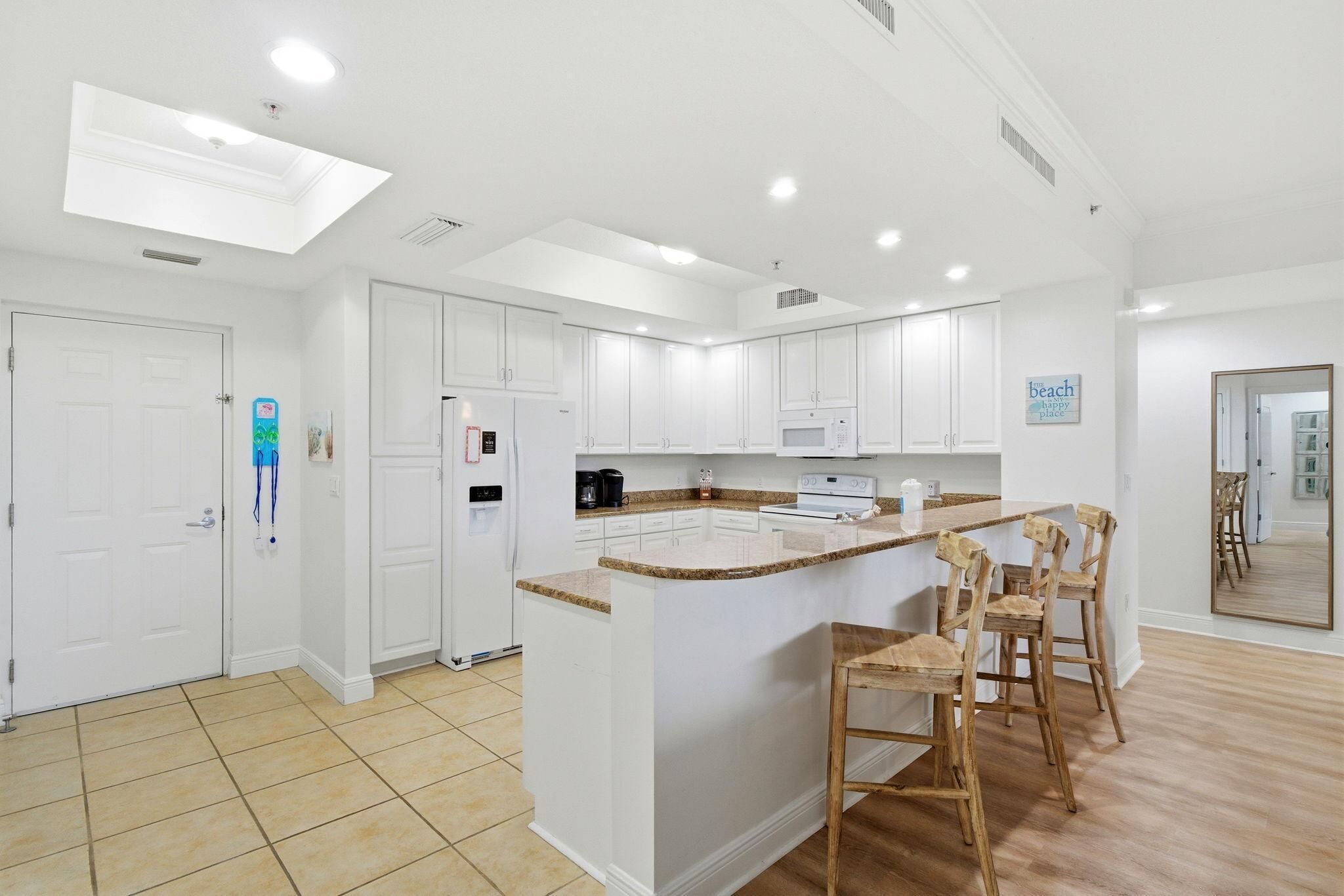 A modern kitchen with white cabinets, a central island with bar stools, and a microwave above the island.